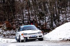 a white car driving down a snow covered road next to trees and people in the background