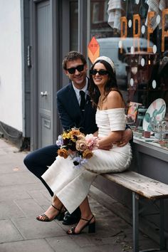 a man and woman sitting on a bench in front of a store window with their arms around each other