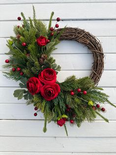 a wreath with red roses and greenery hanging on a white wooden wall next to a door