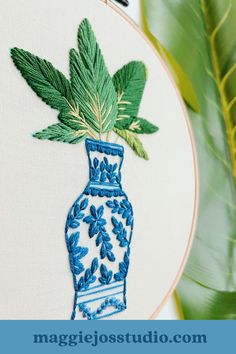 a blue and white vase with green leaves in it on a table next to a plant