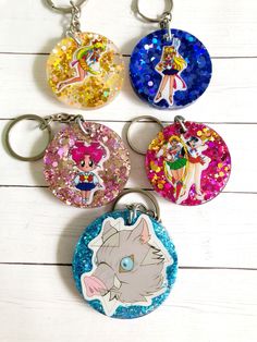 four keychains with cartoon characters on them sitting on a white wooden surface,