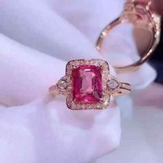 a pink diamond ring sitting on top of a white cloth next to a pair of gold rings