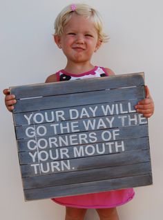 a child holding a sign that says your day will go the way the corners of your mouth turn