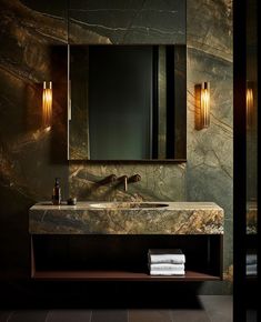 a bathroom vanity with marble counter top and gold lights on the wall above it, next to a mirror