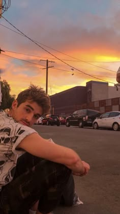 a young man sitting on the ground next to a skateboard in front of a parking lot