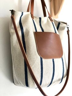 a white and blue striped bag hanging on a wall next to a coat rack with a brown leather handle