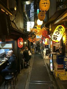 an alley way with people sitting at tables and signs hanging from the ceiling in front of them