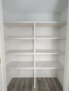 an empty closet with white shelving and wood flooring in the middle of it