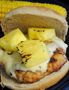 a chicken sandwich with pineapple slices on it and some corn on the cob