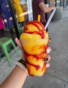 a person holding up a cup with ice cream and fruit in it on the street