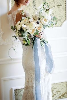 a woman in a white dress holding a bouquet of flowers and a blue ribbon around her waist