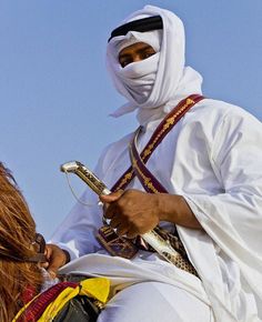 a man dressed in white sitting on top of a horse next to another person with a cell phone