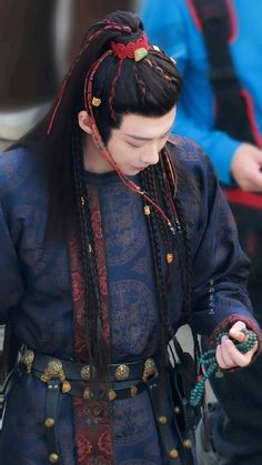 a woman with long braids is looking down at her cell phone while wearing a blue dress