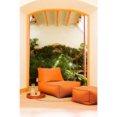 an orange chair and ottoman on the floor in front of a doorway with plants behind it