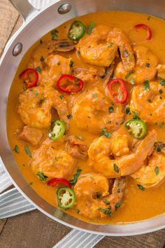 a pan filled with shrimp and peppers on top of a wooden table next to a napkin