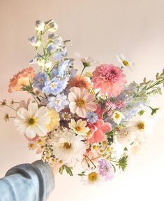 a person holding a bouquet of flowers in their hand with the wall behind them painted pink, blue and white