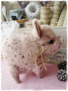 a small stuffed pig sitting on top of a pink table next to a pine cone