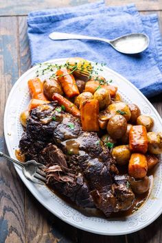 a white plate topped with meat and potatoes on top of a wooden table next to a blue towel