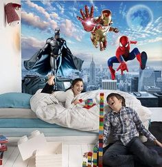 two children are playing on the floor in front of a wall mural with superheros and spider - man