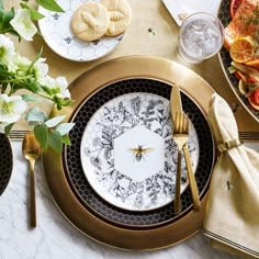 the table is set with plates, silverware and gold utensils on it