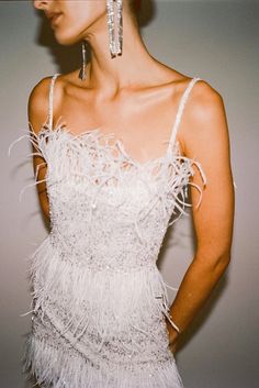 a woman in a white dress with feathers on her head and one hand on her hip