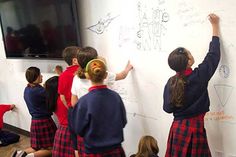 several children writing on a whiteboard in front of a group of other kids wearing school uniforms