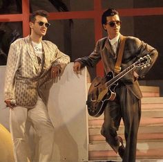 two men in suits and sunglasses are standing next to each other with an electric guitar