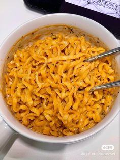 a white bowl filled with noodles on top of a table next to a cell phone