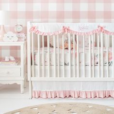 a pink and white baby's room with checkered wallpaper, crib bedding, nightstands and dresser