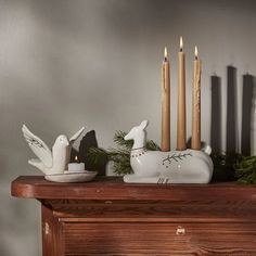 some candles are sitting on top of a mantle with birds and pine branches in front of them