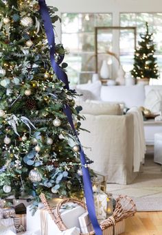 a decorated christmas tree in a living room with blue ribbon on the top and presents under it