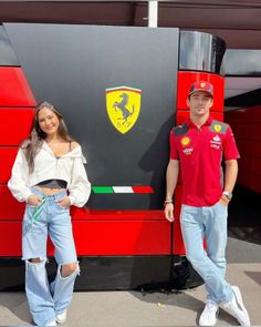 two people standing in front of a large red car with the ferrari logo on it