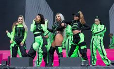 the girls are dressed in neon green and black outfits on stage at an outdoor concert