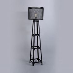 a tall black metal floor lamp with a mesh shade on it's top and two candles in the bottom