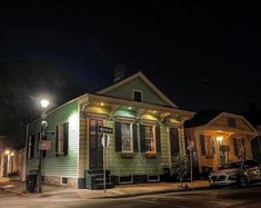 a small green house sitting on the corner of a street at night with lights on