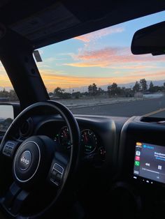 the inside of a vehicle with dashboard, steering wheel and display screen showing sunset or sunrise