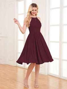 a woman in a maroon dress standing on a wooden floor with her hand up to the side