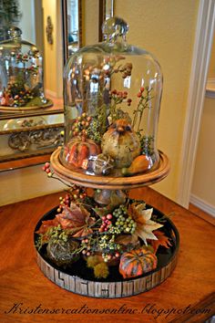 a wooden table topped with a glass clochet covered in autumn decorations