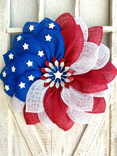 an american flag wreath hanging on the side of a white wooden door with red, white and blue flowers