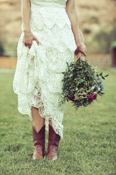 a woman in a white dress holding a bouquet of flowers and wearing cowboy boots on the grass