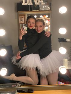 two women in tutu skirts are taking a selfie with their cell phone while standing in front of a mirror