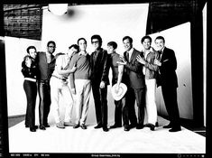 a group of people standing next to each other in front of a white wall with one man holding a hat