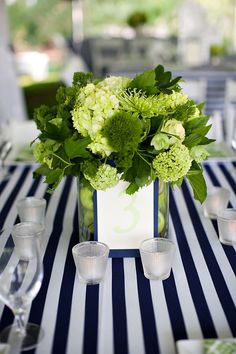 there is a vase with green flowers in it on top of a striped table cloth