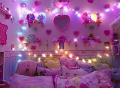 a bedroom decorated in pink and purple with teddy bears on the wall, lights strung from above