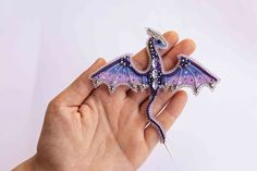 a hand holding a purple and blue dragon brooch on it's left side