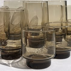 several glasses are lined up on a white table cloth, with one empty glass in the middle