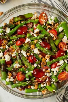 a glass bowl filled with asparagus, cherry tomatoes and feta cheese on top