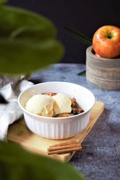 a bowl filled with ice cream sitting on top of a cutting board next to an apple