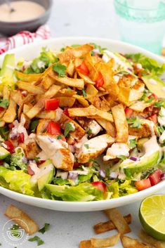 a salad with chicken, lettuce and tomatoes in a white bowl on a table