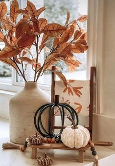 a vase filled with leaves and pumpkins on top of a table next to a window